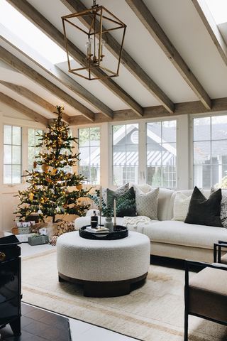 Neutral, modern living room with a lit Christmas tree in the corner and presents under the tree