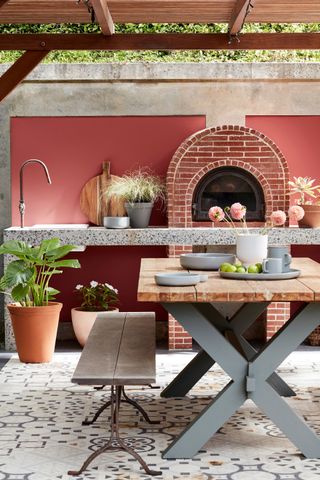 An outdoor kitchen with a brick pizza oven, sink and wooden table and bench