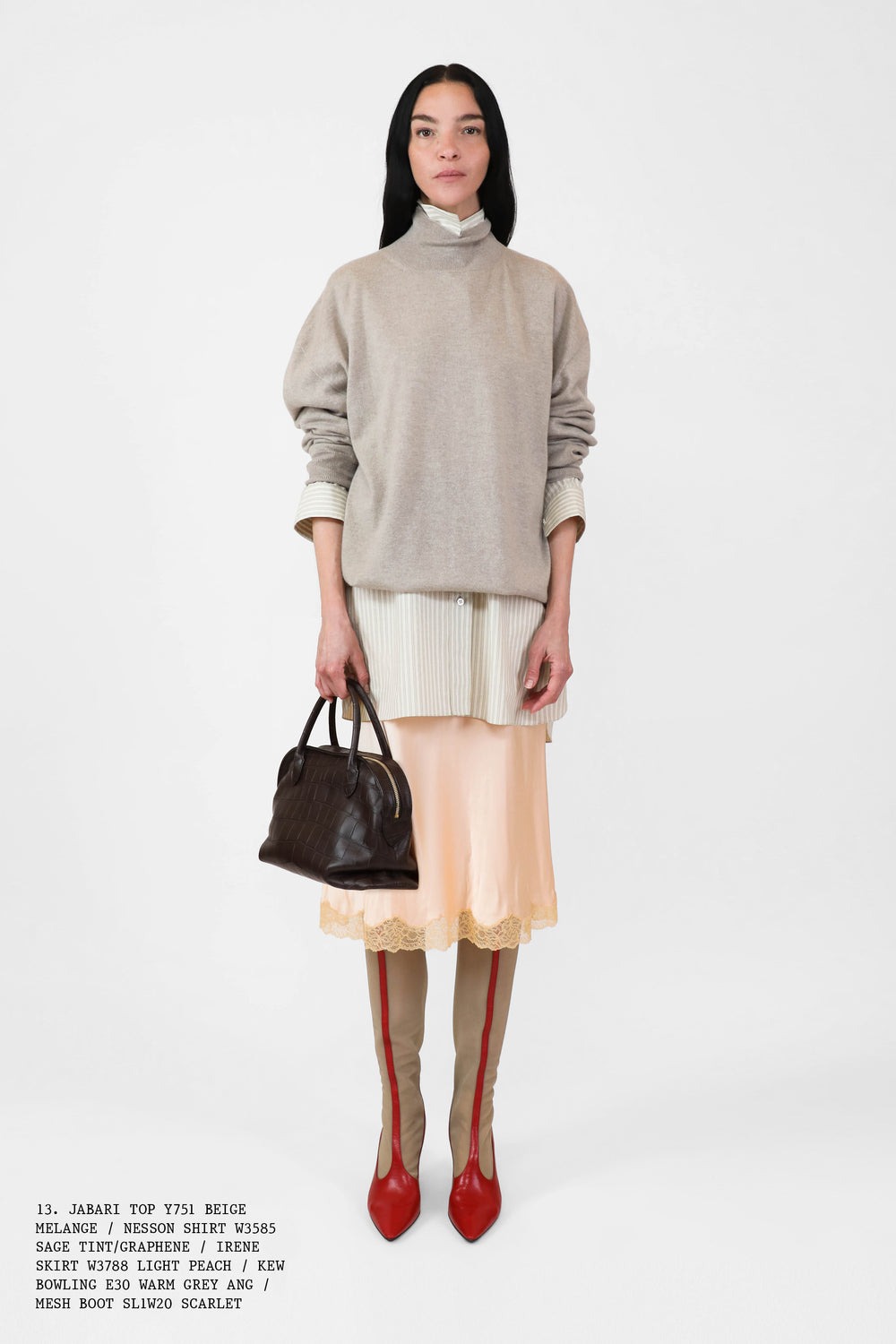 A The Row model from the spring 2025 lookbook wearing a sweater over a shirt, pink lace-trim skirt, and red boots.
