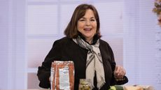 Ina Garten cooking in kitchen. She is a white lady with a brown bob, pictured in a black shirt and cream scarf