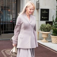 Pamela Anderson steps outside wearing tights with open-toe sandals and a knee-length skirt.