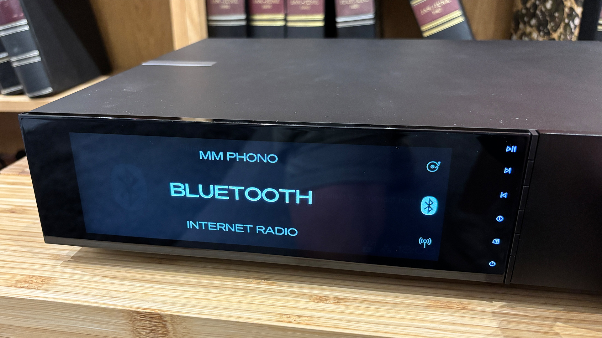 Cambridge Audio Evo 300 all-in-one system on wooden hi-fi rack in front of bookcase, on display are source options