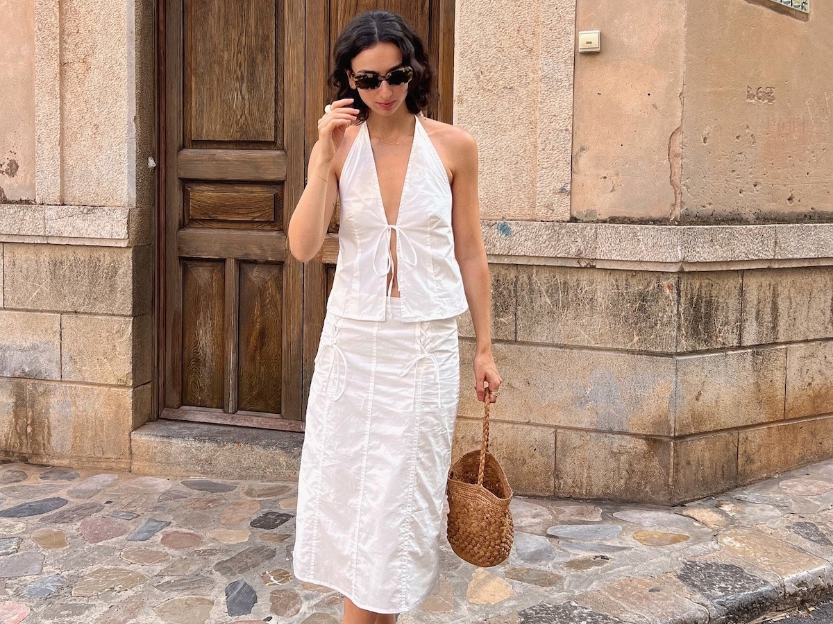 Woman wearing a white linen skirt and top holding a woven bucket bag.