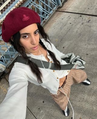 Woman wearing a white cardigan with striped tan shorts and a red cap.