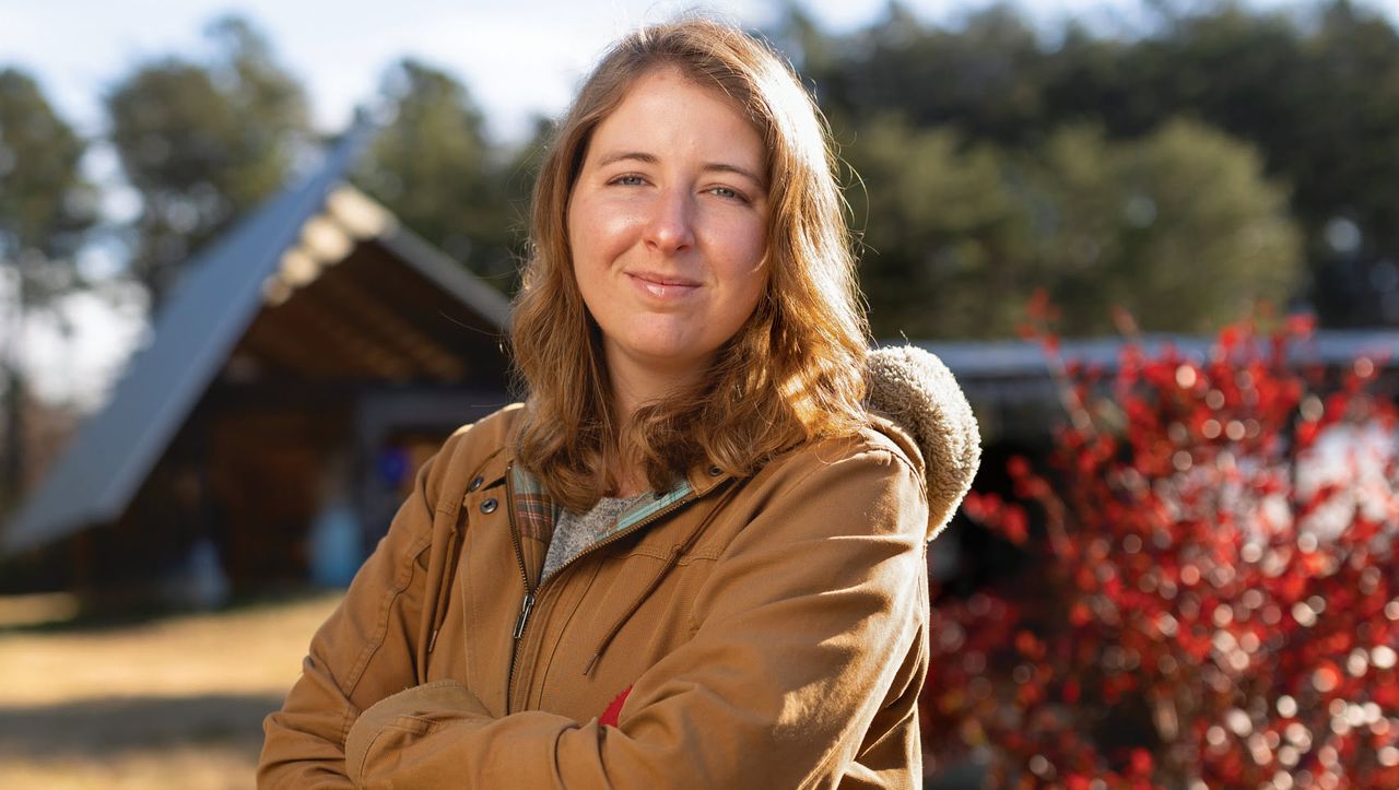 Kristen stands with arms crossed outdoors at the farm