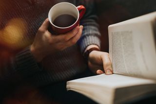 A person holding a cup of coffee while reading a good book.