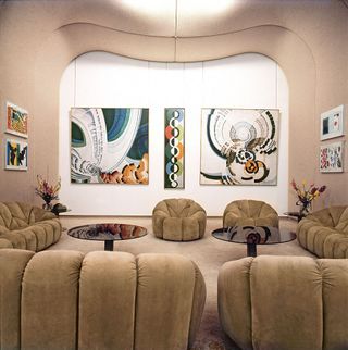Beige squishy sofas and chairs in a beige room with large multi-coloured artwork on the wall
