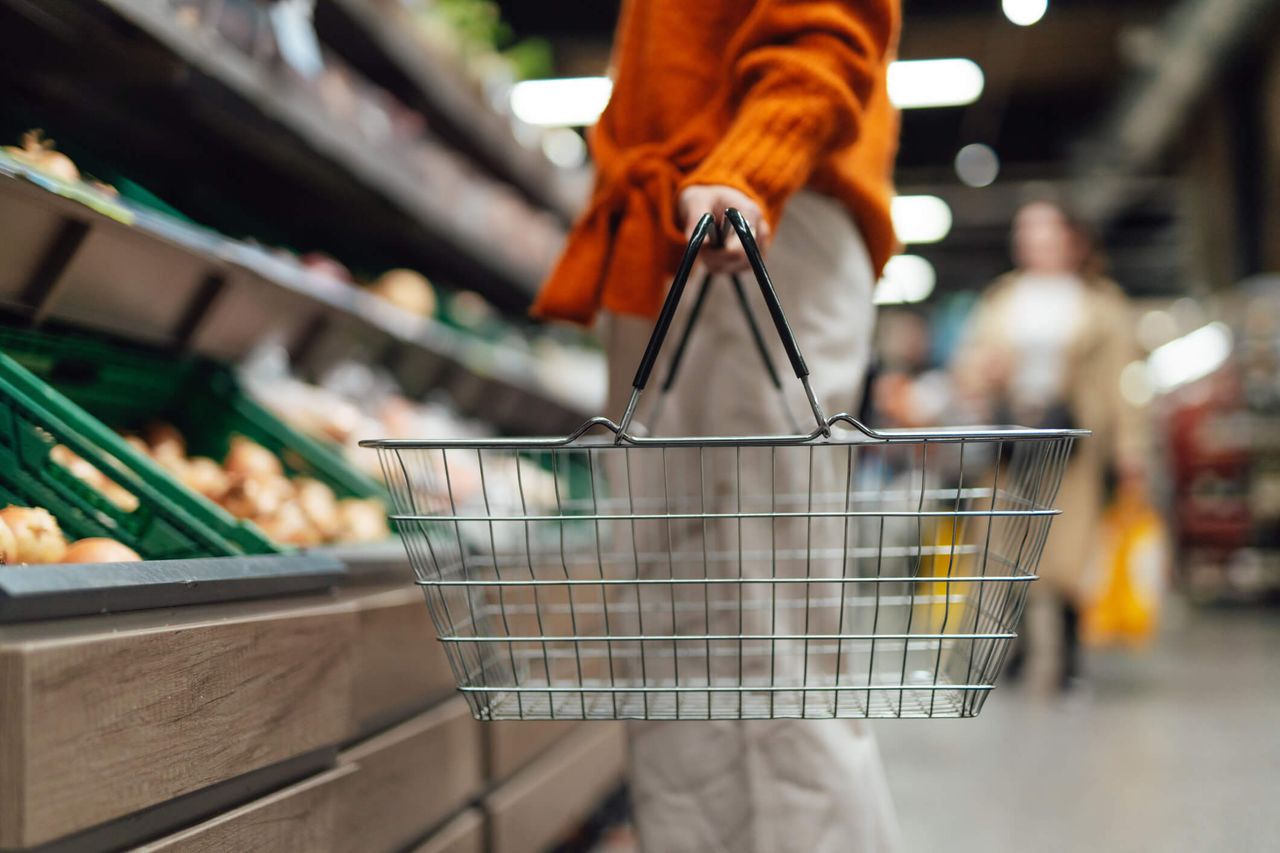 A person holding a basket while shopping in a supermarket.