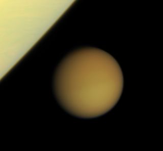 Swathed in its thick blanket of atmosphere, frigid Titan approaches the brilliant limb of Saturn on March 14, 2008.