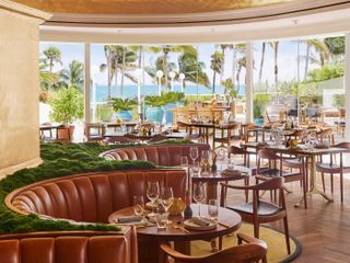 A sea-view dining room of a hotel features mid-century modern wood and leather furniture in brown along with musk-covered seats.