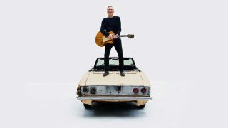 Bryan Adams standing on a Chevy Corvair with his guitar
