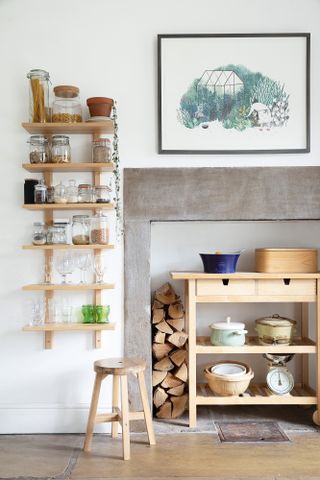 White kitchen with stone fireplace, wooden open shelving for jars and bowls