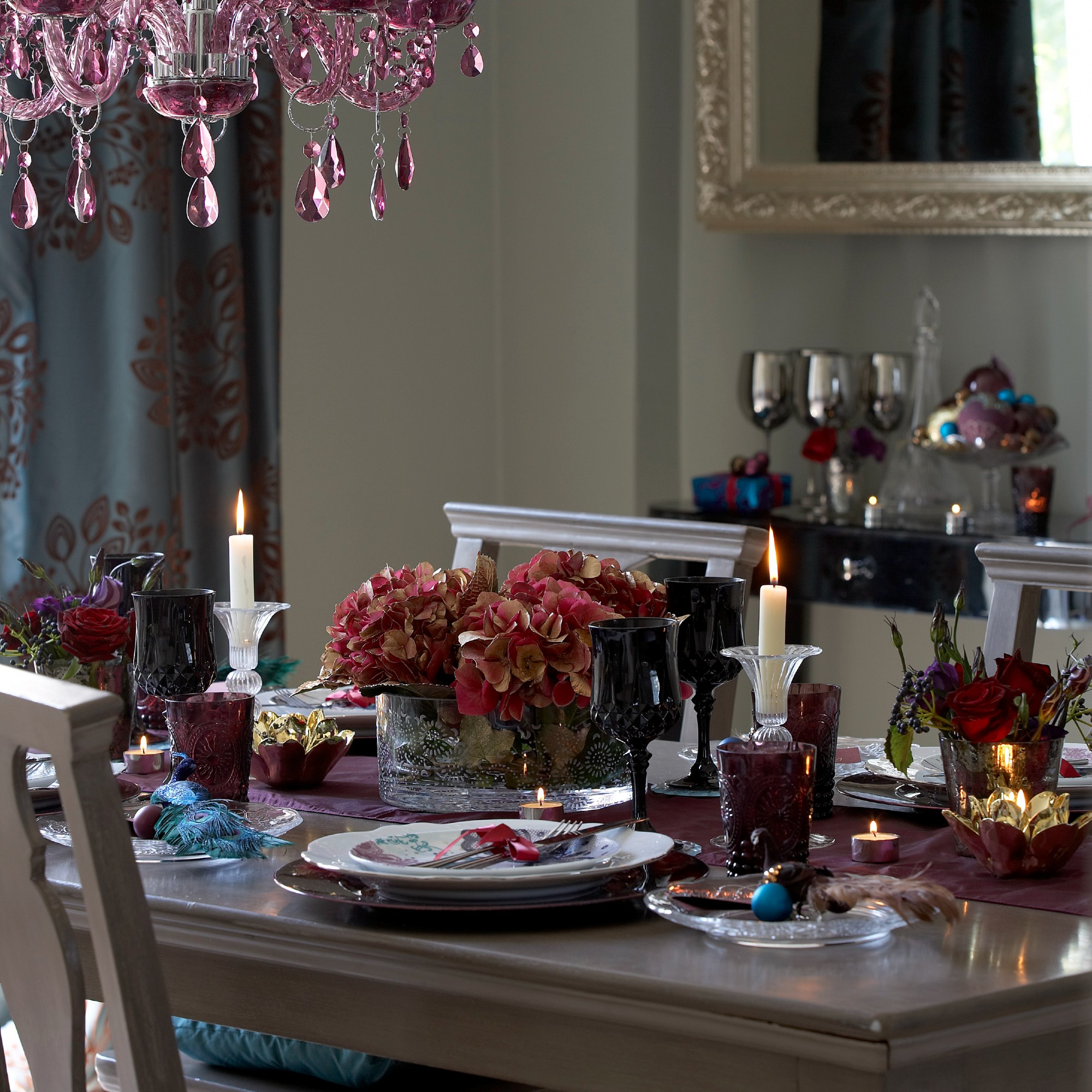 A dining room decorated for Christmas with the table set and decorated with red roses and hydrangeas and a deep purple table runner