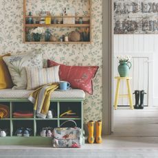 A hallway covered in a botanical wallpaper with a cube shoe bench and various scatter cushions on top