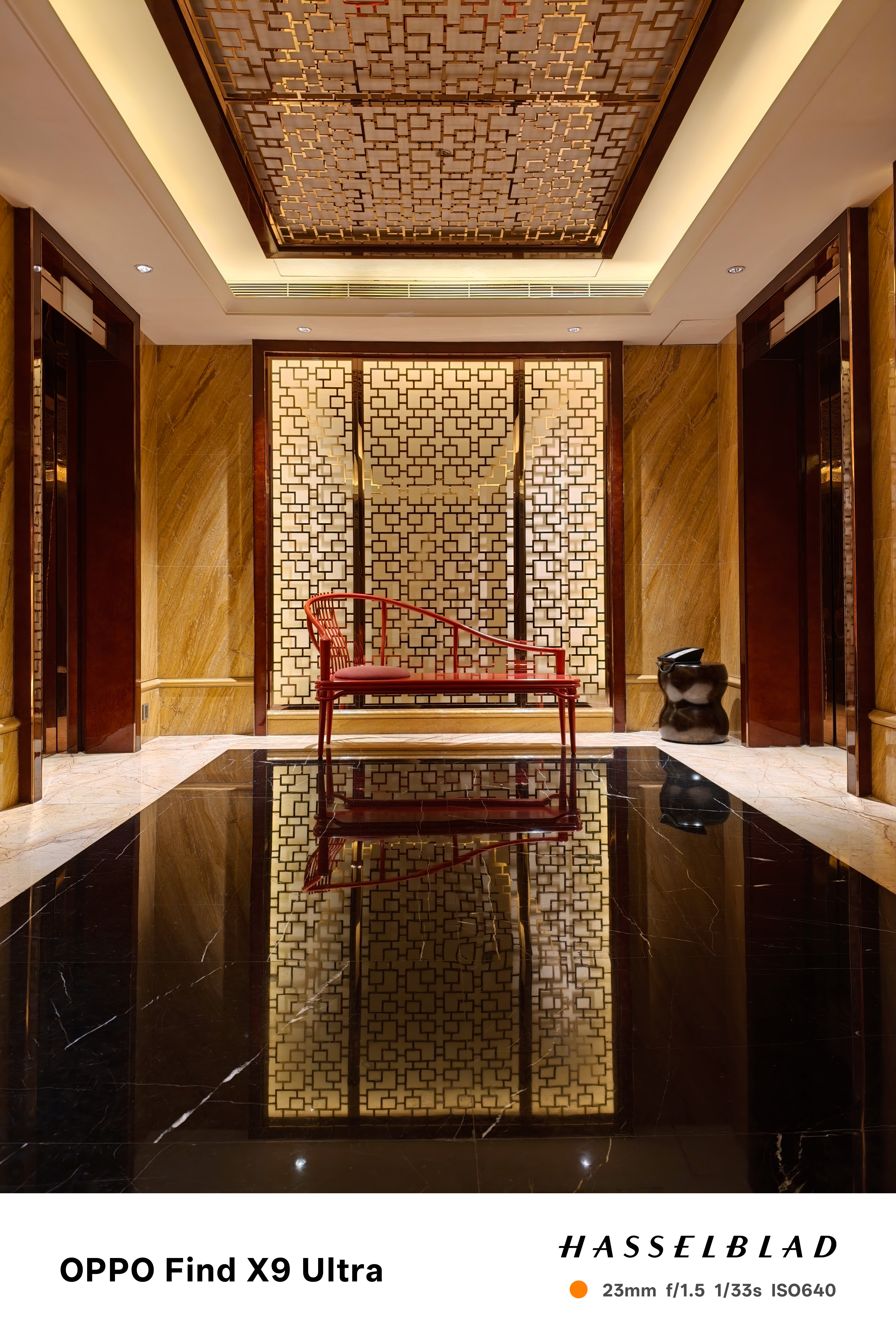 Symmetrical hotel lobby with patterned walls, red chair, and glossy floor reflection