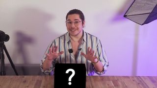 James Artaius standing at a desk with a mystery box bearing a "?" symbol