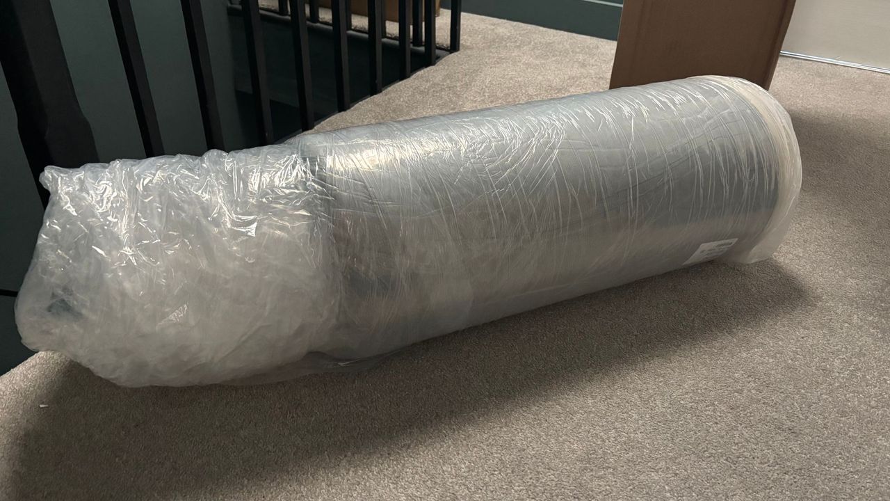 The Birch Plush Organic Mattress Topper compressed and rolled into plastic wrapping.