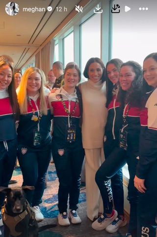 Women of Team USA wearing red, white and blue warm up suits and posing with a service dog and Meghan Markle at an Invictus Games event