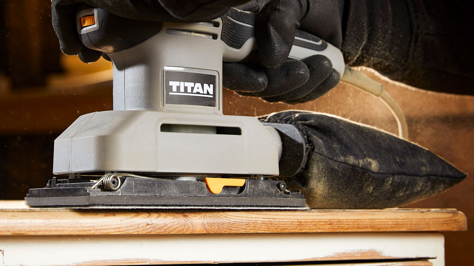 Gloved hand holding Titan sheet sander, sanding table top
