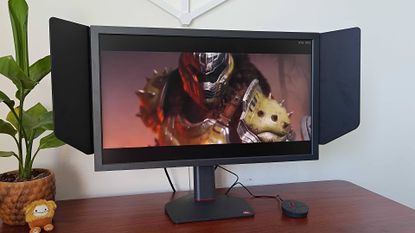 BenQ Zowie XL2586X+ monitor next to plant on desk with DOOM: The Dark Ages cutscene on screen featuring the Doomslayer.