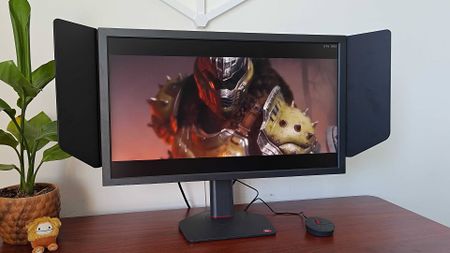 BenQ Zowie XL2586X+ monitor next to plant on desk with DOOM: The Dark Ages cutscene on screen featuring the Doomslayer.