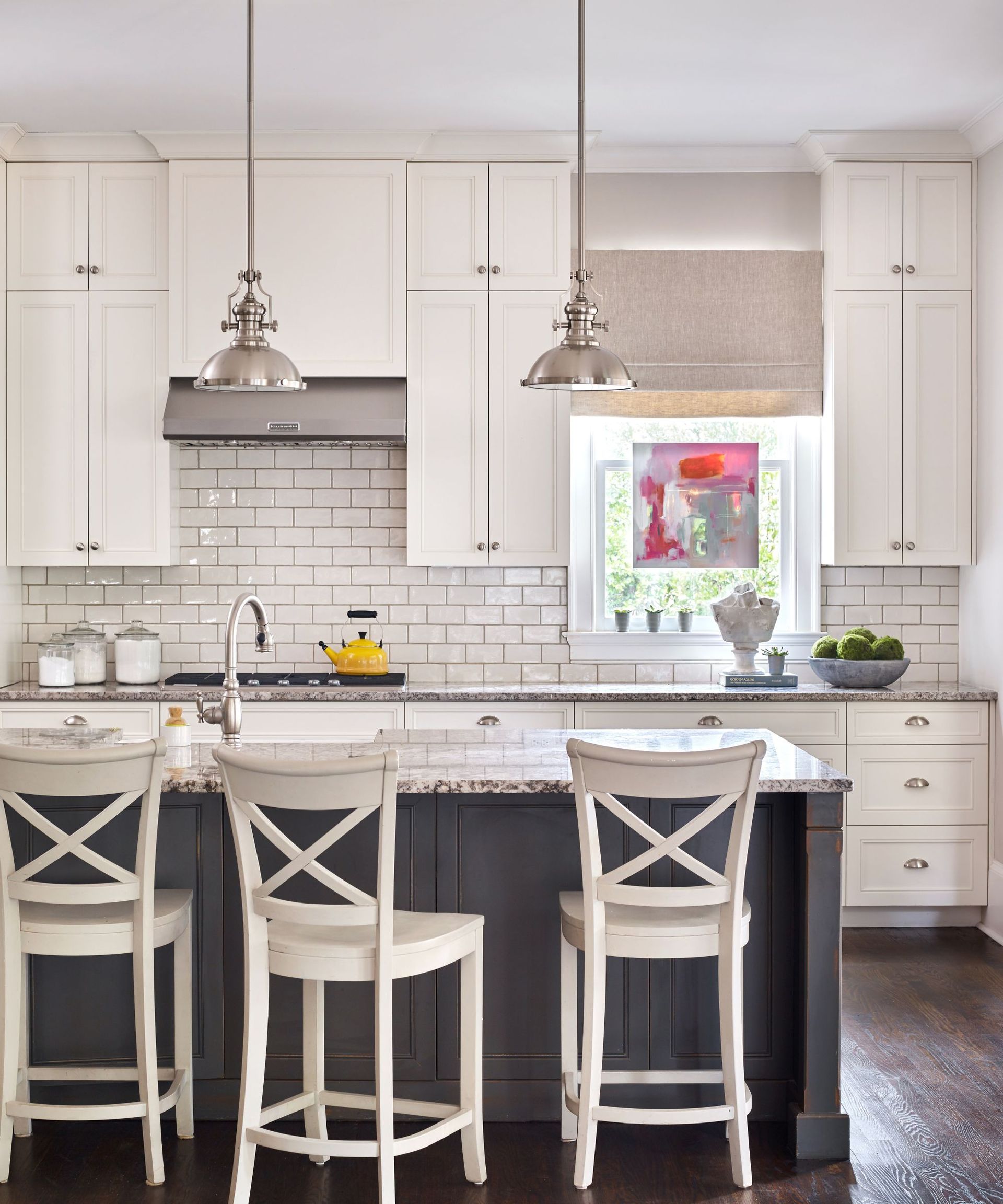 white kitchen units and white cross-backed bar stools on dark wood island and marble countertops and wood flooring