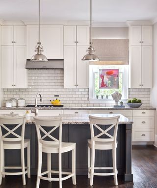 white kitchen units and white cross-backed bar stools at dark wood island and marble countertops and wood flooring