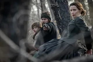 taylor kitsch as isaac pointing a gun in the woods while protecting sara played by betty gilpin and her son played by preston mota in american primeval