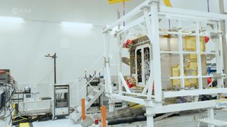 A cubical satellite under assembly in a clean room.