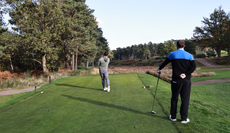 A golfer hits a tee shot while another stands behind him