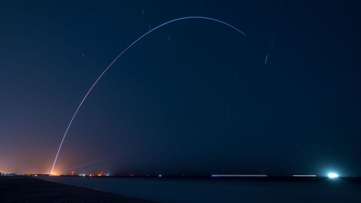 long-exposure photo of a rocket launch at night, showing the vehicle&#039;s path through the dark skies as a curving yellowish streak