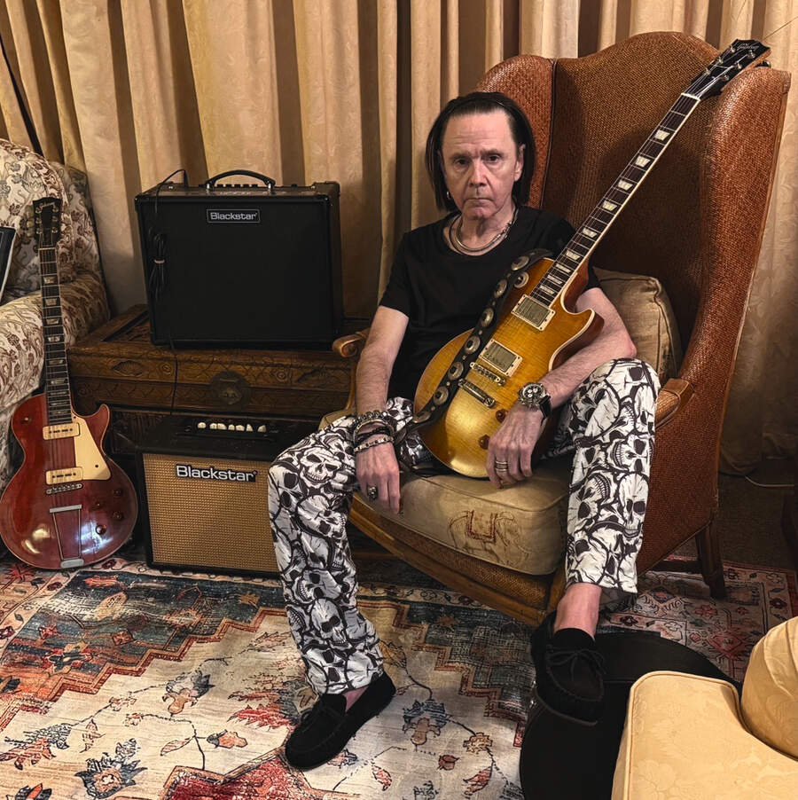 Brian Robertson in a leather chair, holding a Gibson Les Paul