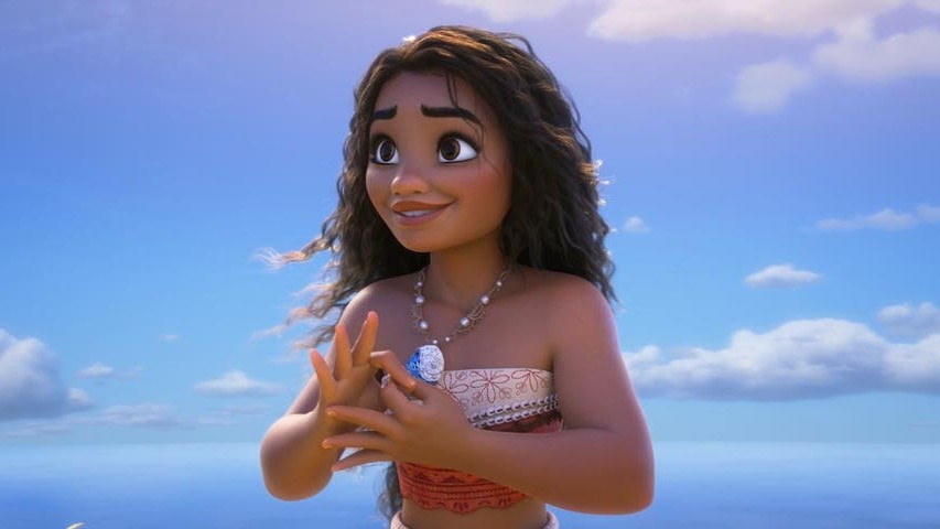 Moana smiles warmly while holding her shell necklace against a bright blue sky and ocean backdrop.