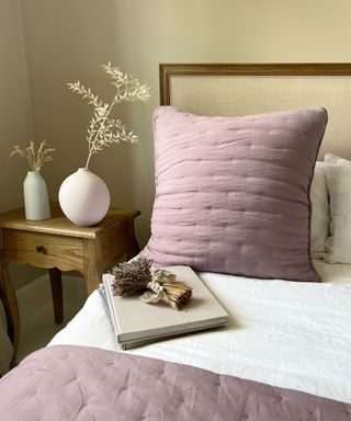 A yellow bedroom with a bed with a purple throw pillow and blanket, and a wooden nightstand