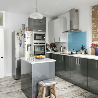 A white walled kitchen with grey units, white countertops, and a blue splashback