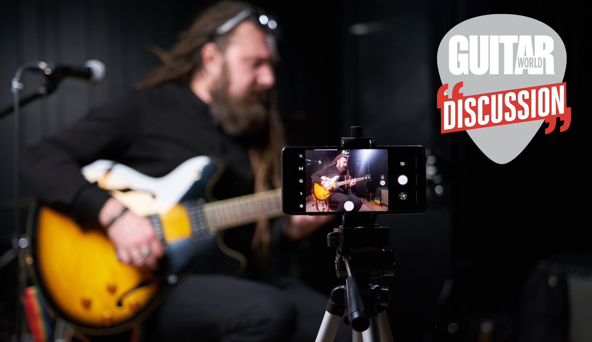 A man is filmed by his iPhone on a tripod playing an electric guitar