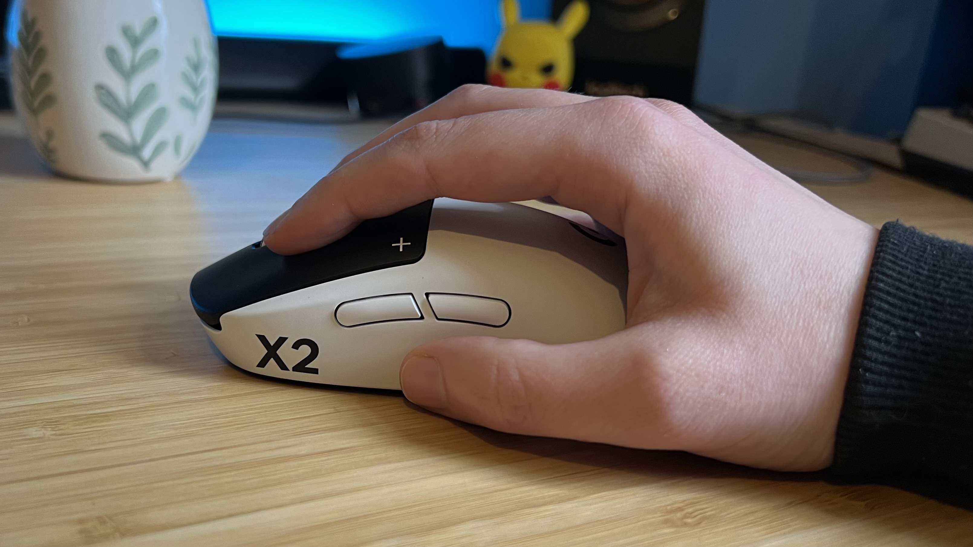Hand using the Logitech G Pro X2 Superstrike gaming mouse in a claw grip on a wooden desk