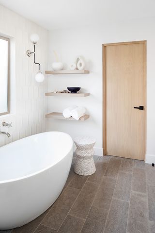 A neutral bathroom with curved bath and shelving