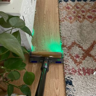 Dyson V12 Detect Slim Absolute in action on wooden flooring, with the laser showing lots of dust on the floor