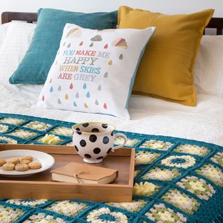 bed with designed cushion wooden tray with cup cookie and book