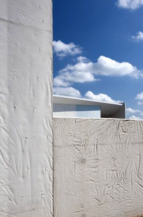 Hearning Museum of Contemporary Art by Steven Holl, Denmark. The side of a building with rough white walls and a blue sky and clouds behind it.