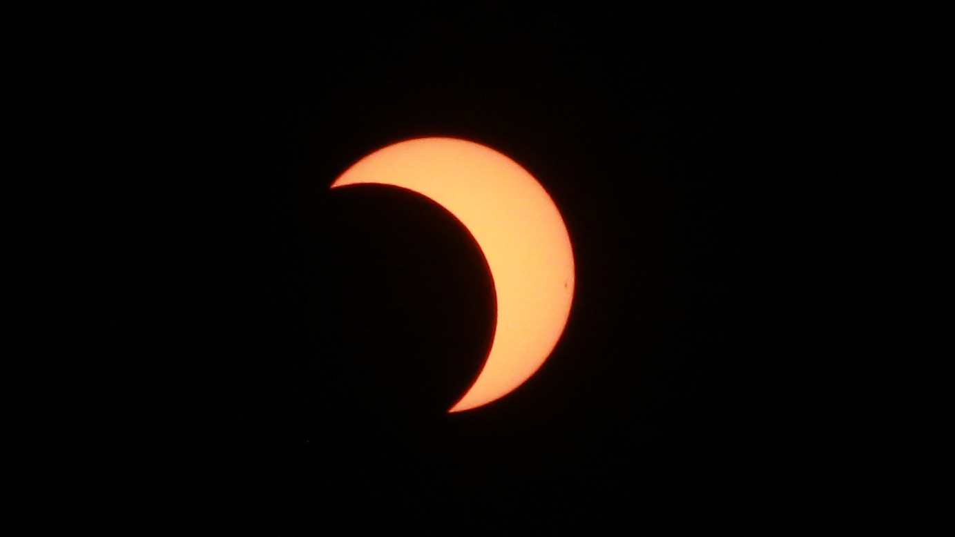 The solar disk is shown with its right side covered by the moon's silhouette against a black sky during an eclipse.