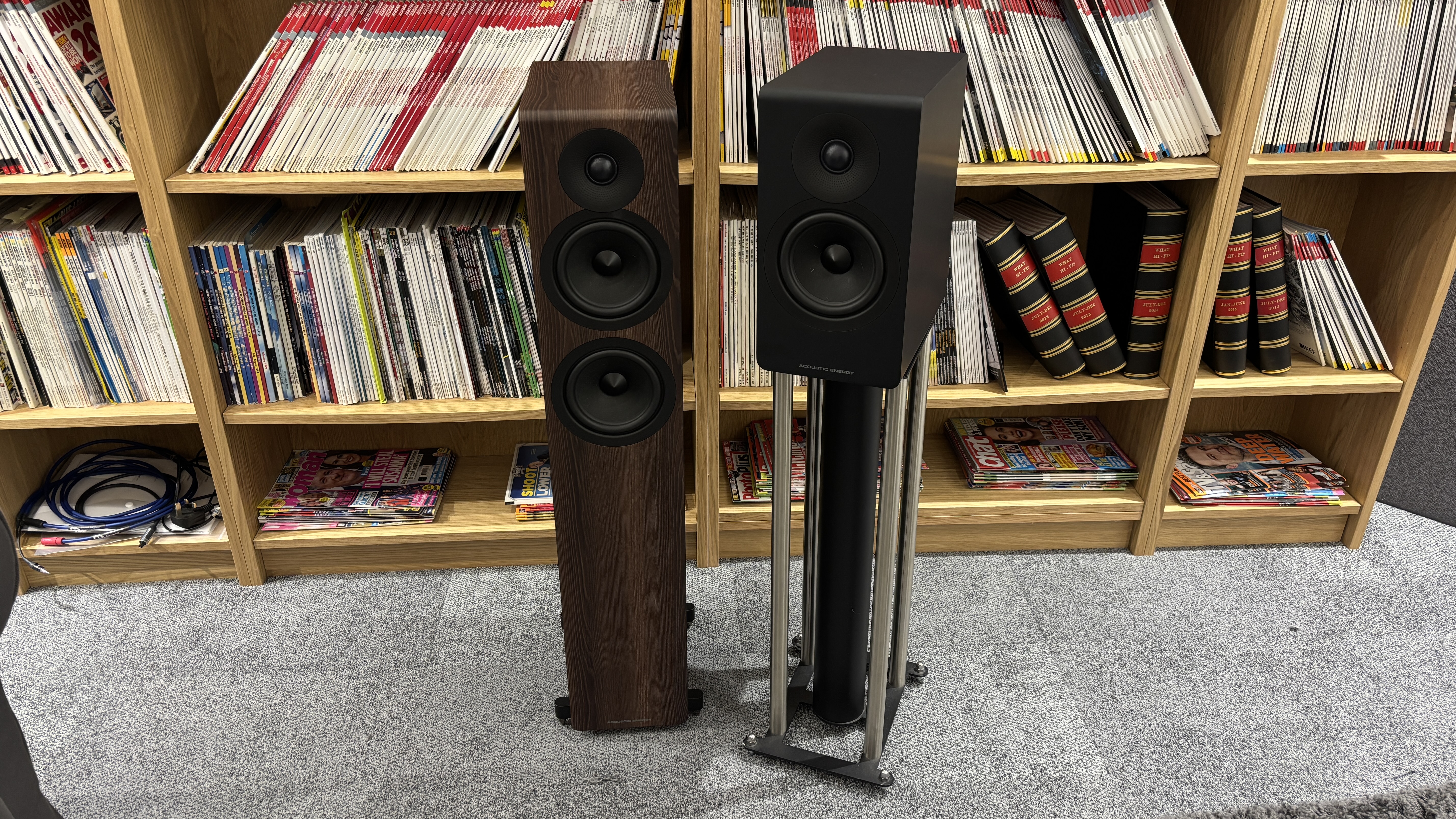 Acoustic Energy AE309 Mk2 and AE300 Mk2 stood next to each other in front of bookshelves filled with magazines