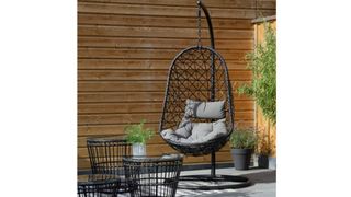 the Dawsons Living Vienna Hanging Egg Chair in a garden with a fenced wall, stone floor, and plant pots