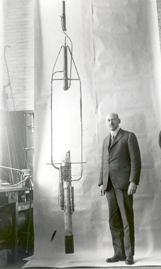 Space pioneer Dr. Robert H. Goddard stands with his rocket with the double-acting engine in November 1925, following more than two years of pump development based on the idea of a separate pump for each propellant, a significant advance.