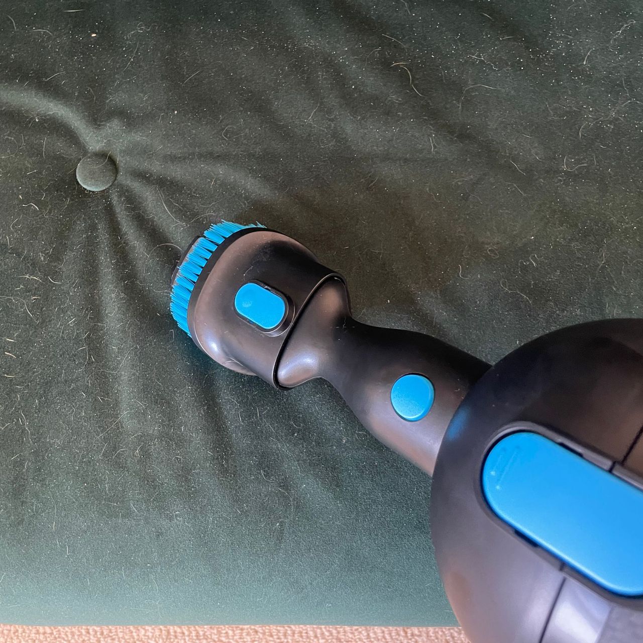 Using the upholstery tool on a green velvet sofa bed covered in hair