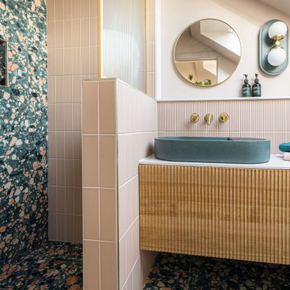 pale pink bathroom with wooden sink cupboard underneath circular mirror