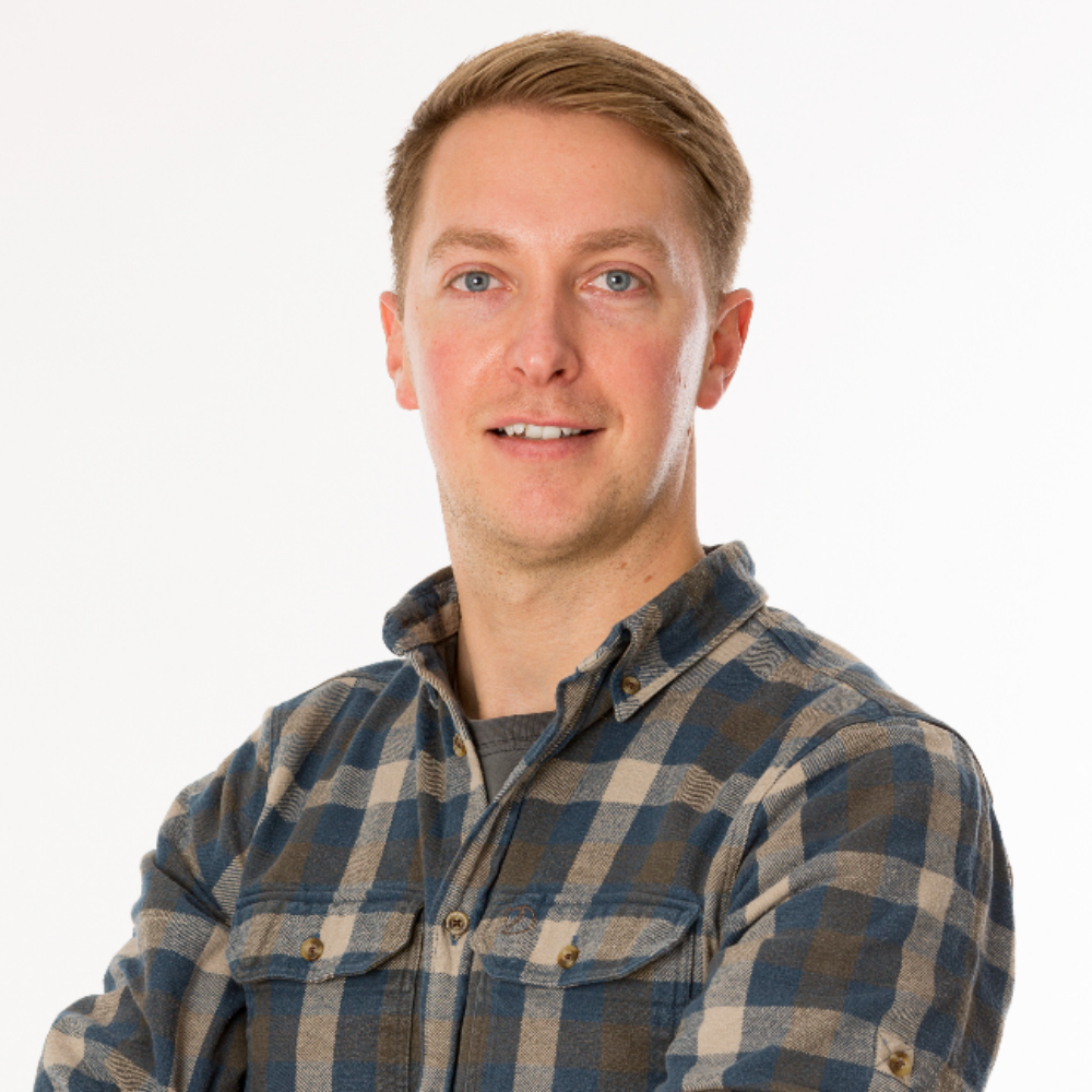 A blonde man in a flannel shirt smiling at the camera.