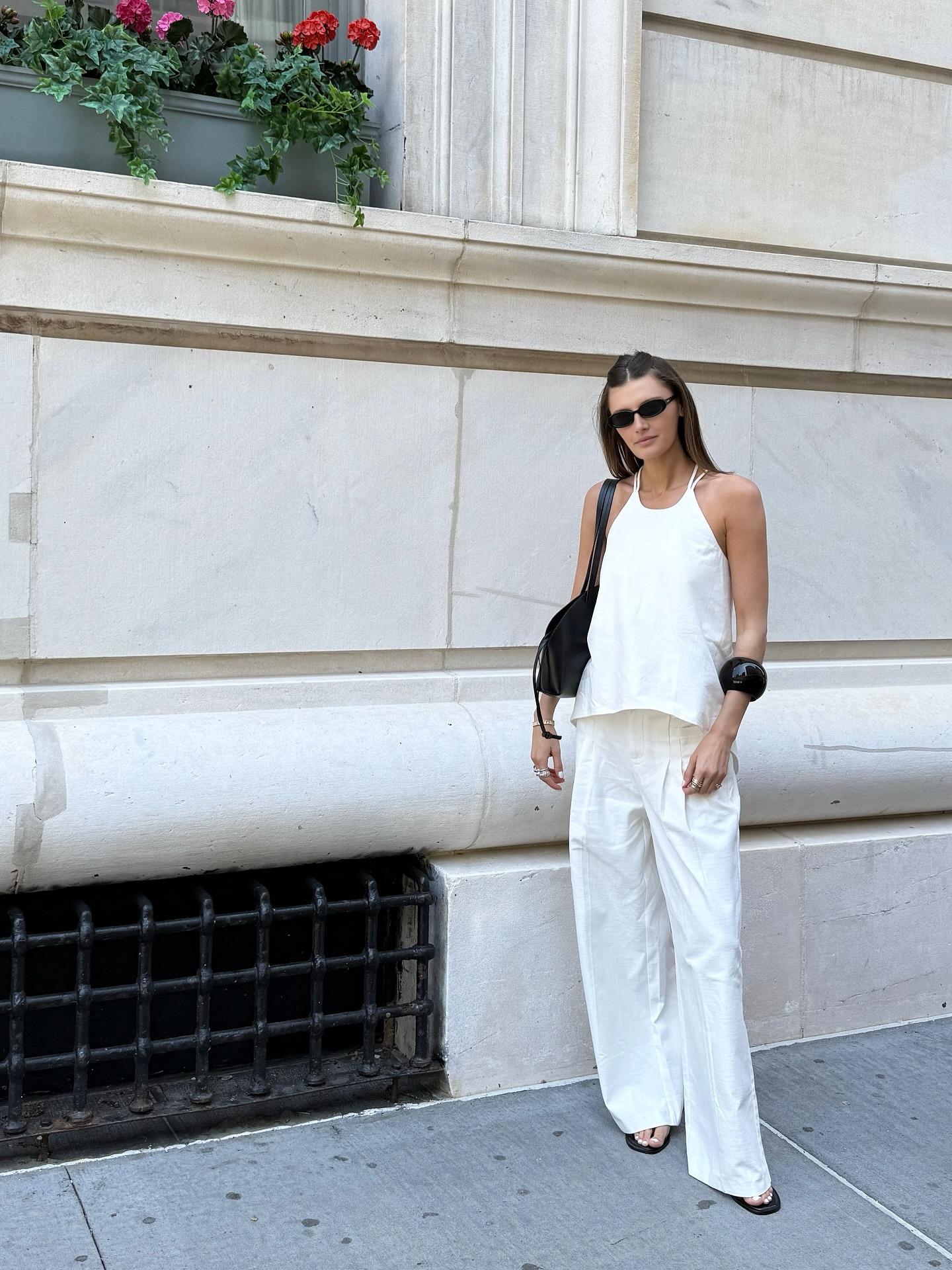 A woman wearing all white with a black arm cuff, black bag, and black sunnies.