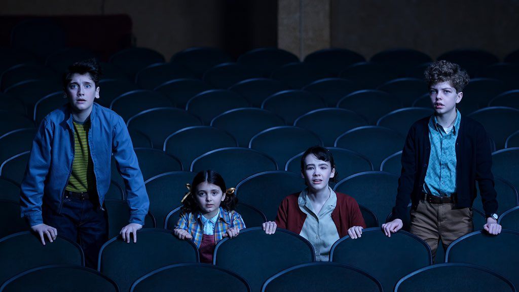 Four children stand in a theater looking scared